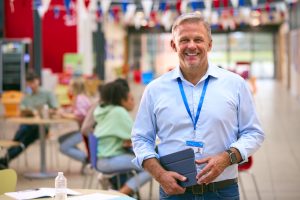 Smiling Male University Teacher Tutor Or Lecturer Inside College Building With Digital Tablet